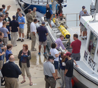 The attendees stand on the pier next to the Meriel R. loaded with the AUV.