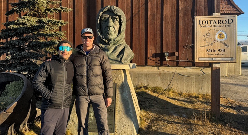 Kaan Cav (left) and Andrew Niedbala (right) pose with Iditarod sign on Nome, AK.